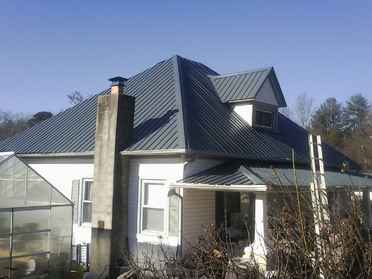 Dark blue standing seam metal roof on a white farmhouse with dormer — Slate & Tile Roof Repair by Roofing Brothers in Houston